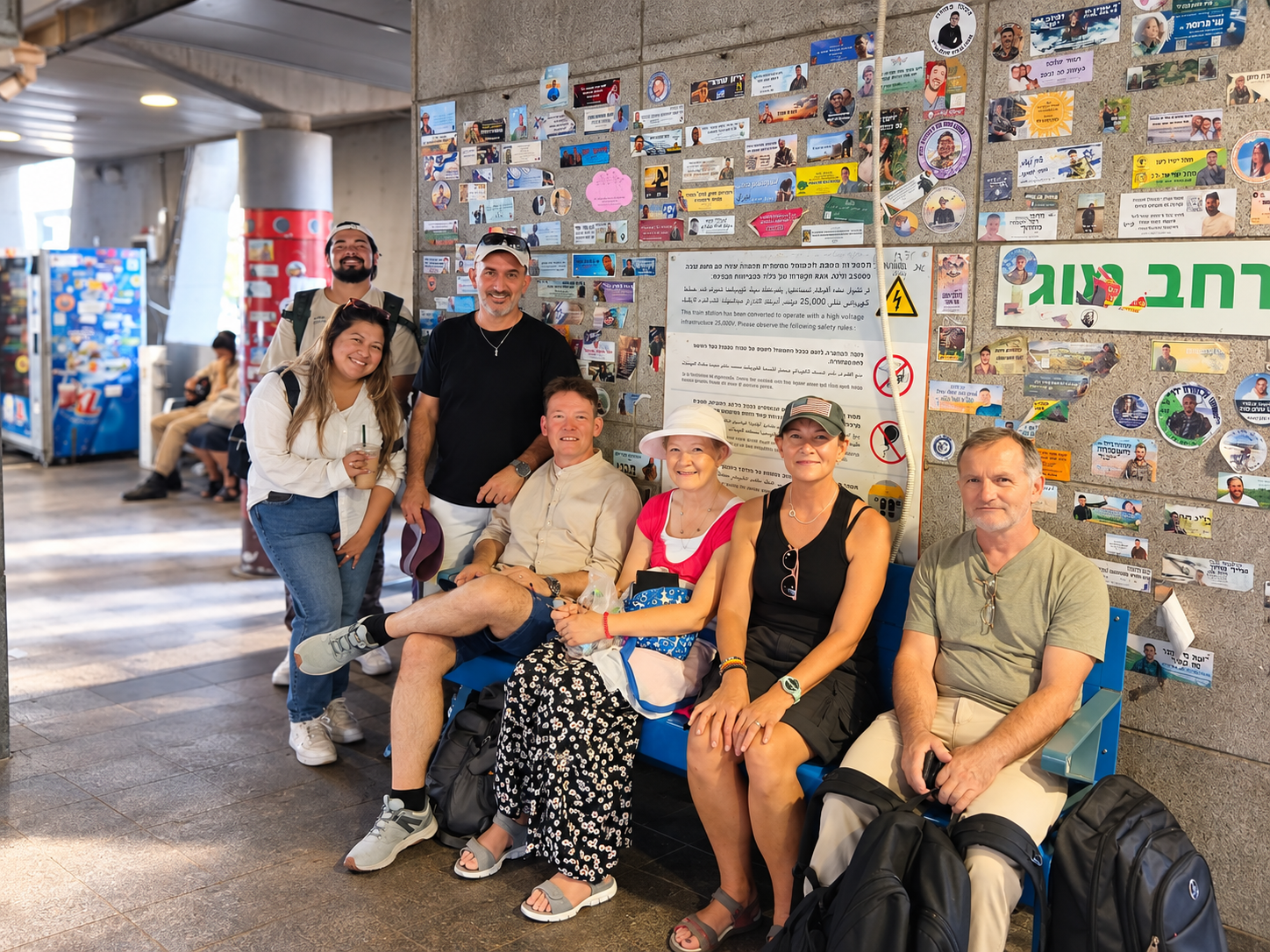 KBN volunteers and friends gathered at a train station beneath a wall covered in stickers.